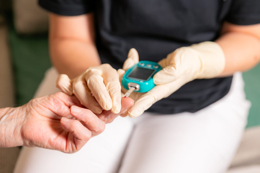 Krankenschwester beim Blutzuckermessen bei einer Patienten in der Hauskrankenpflege