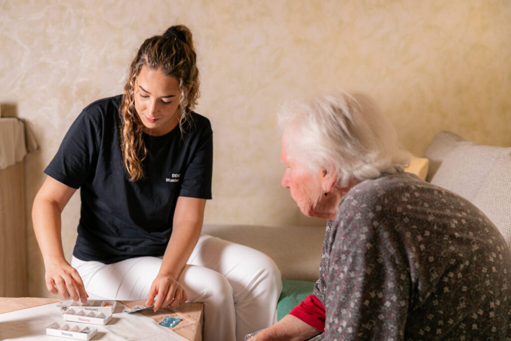 Krankenpflegerin Iris im Wohnzimmer mit Patientin zum Vorbereiten der Medikamente